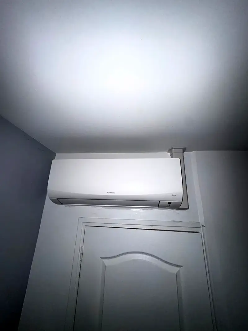 Climatiseur mural Daikin posé au-dessus d’une porte, liaisons cachées sous une goulotte discrète